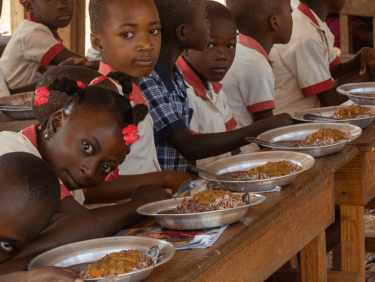 Kinder sitzen an der Schulbank und essen aus Tellern