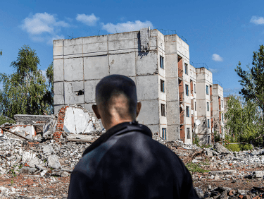 Mann mit dem Rücken zum Bild vor zerstörten Gebäuden